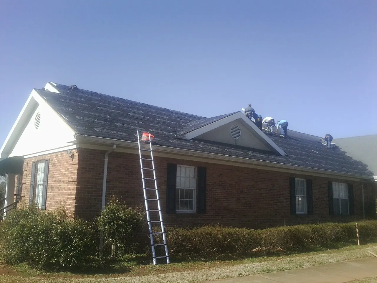 Crew tearing shingles off a brick ranch roof with a ladder set — Metal Roof Repair work by our crew in Wanaque