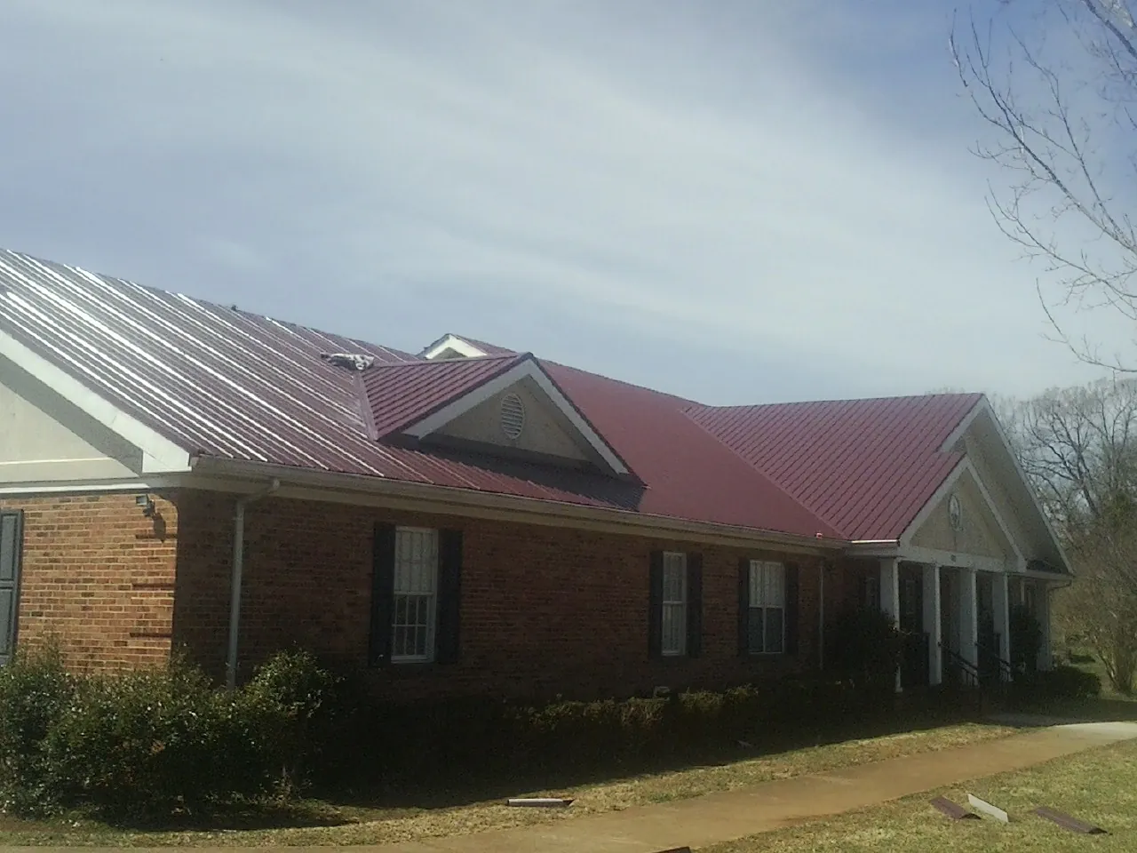 Red metal roof with gabled entries on a long brick building, from a Hail Damage Roof Repair job in Wanaque