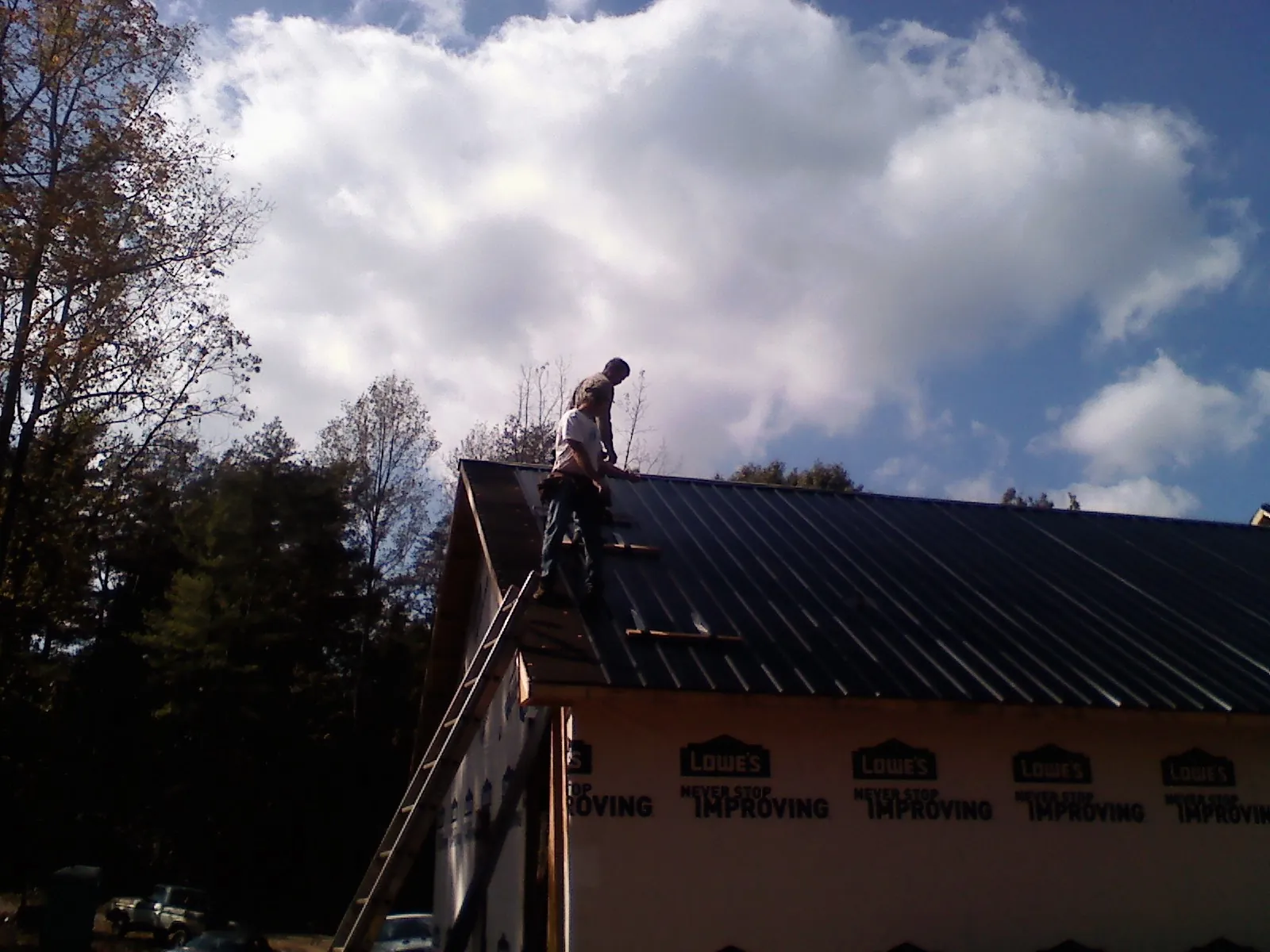 Roofer fastening dark metal panels high against a cloudy sky, from a Roof Inspection job in Wanaque